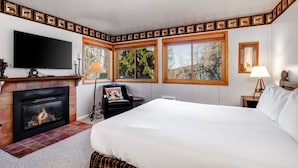 A hotel room with a fireplace, a bed, a TV, and three windows offering a view of trees. - Snow Flower 012 2 Bedroom Condo by RedAwning (Park City)