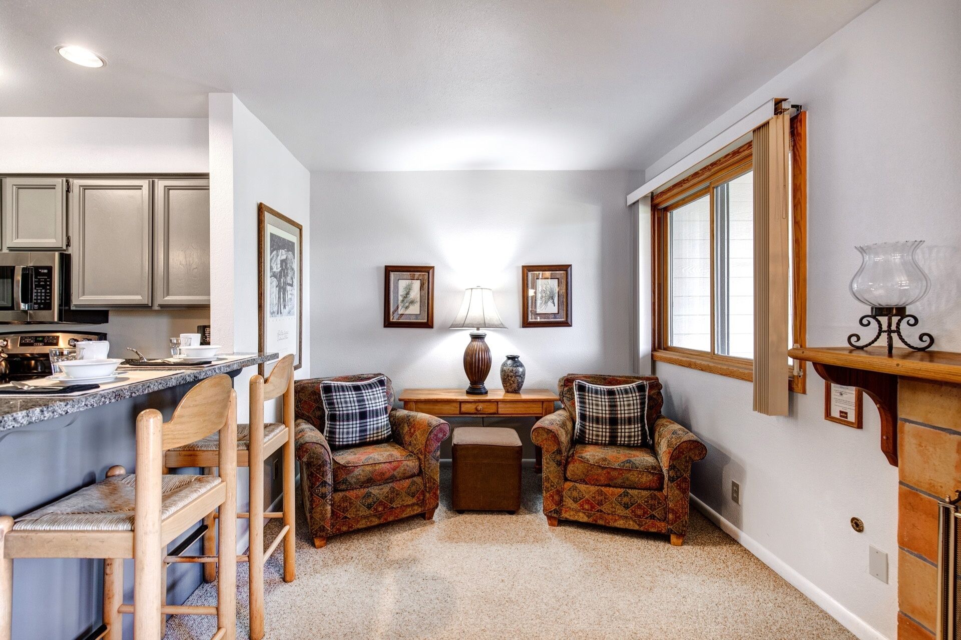 A compact living space with a kitchen, two armchairs, a small table, and a fireplace.