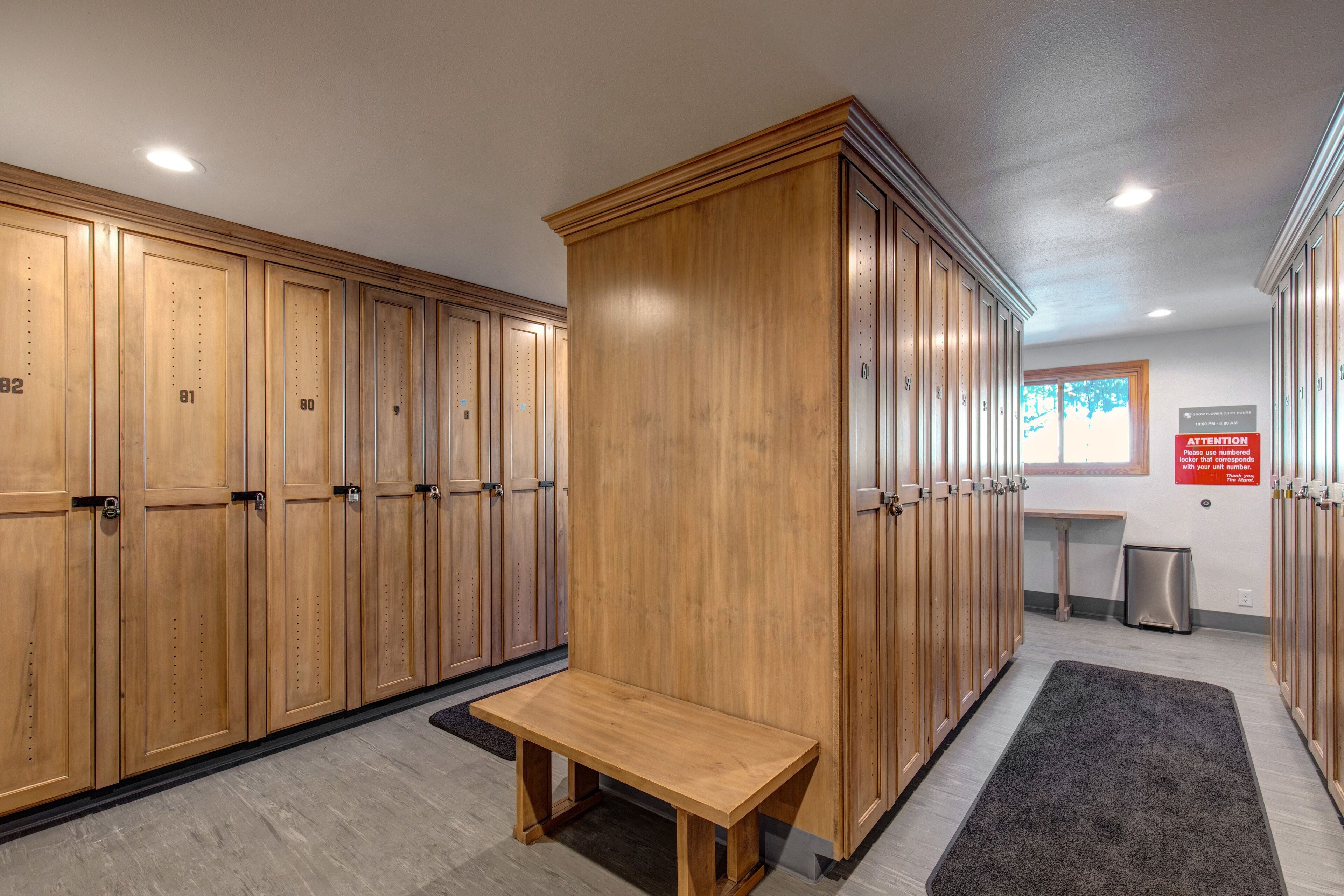 Vestuario con taquillas de madera, un banco y un cubo de basura.