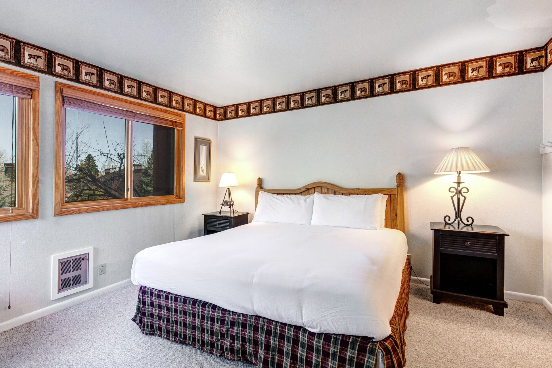 A bedroom with a large bed, two bedside tables with lamps, a window with blinds, and a decorative border with animal pictures.
