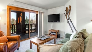 A living room with a sliding glass door leading to a balcony, a television mounted on the wall, and a pair of skis leaning against the wall. - Snow Flower 012 2 Bedroom Condo by RedAwning (Park City)