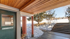 A wooden covered entrance to a building with a sign reading "LOCKER ROOM" and a view of a snowy landscape with stairs leading up to a building. - Snow Flower 012 2 Bedroom Condo by RedAwning (Park City)