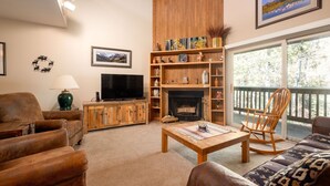 A cozy living room with a fireplace, wooden shelves, a television, and a view of the outdoors. - Snow Flower 159 2 Bedroom Condo by RedAwning (Park City)