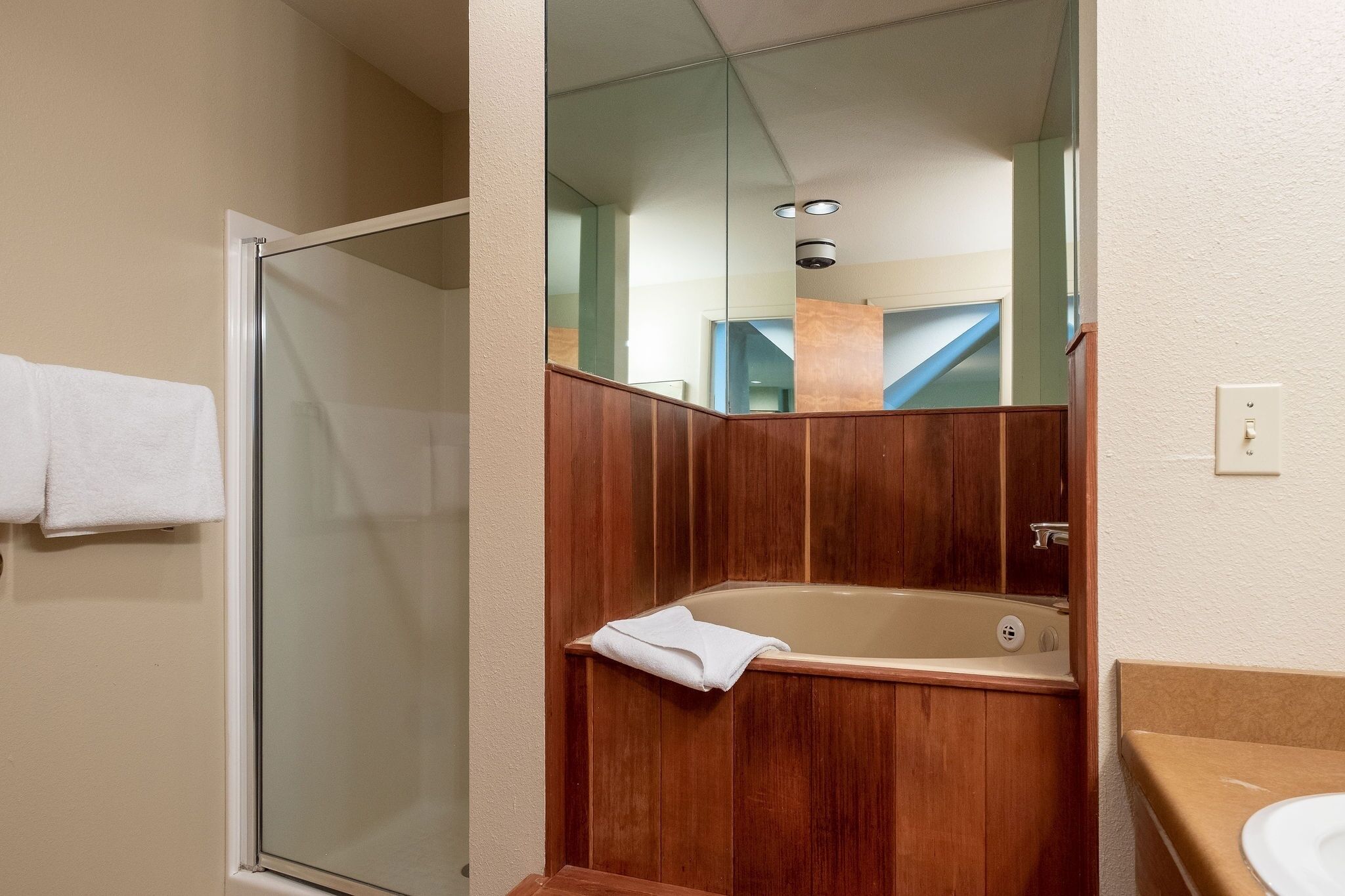 Een badkamer met een glazen douchecabine, een houten badkuip en een wit wastafelmeubel.