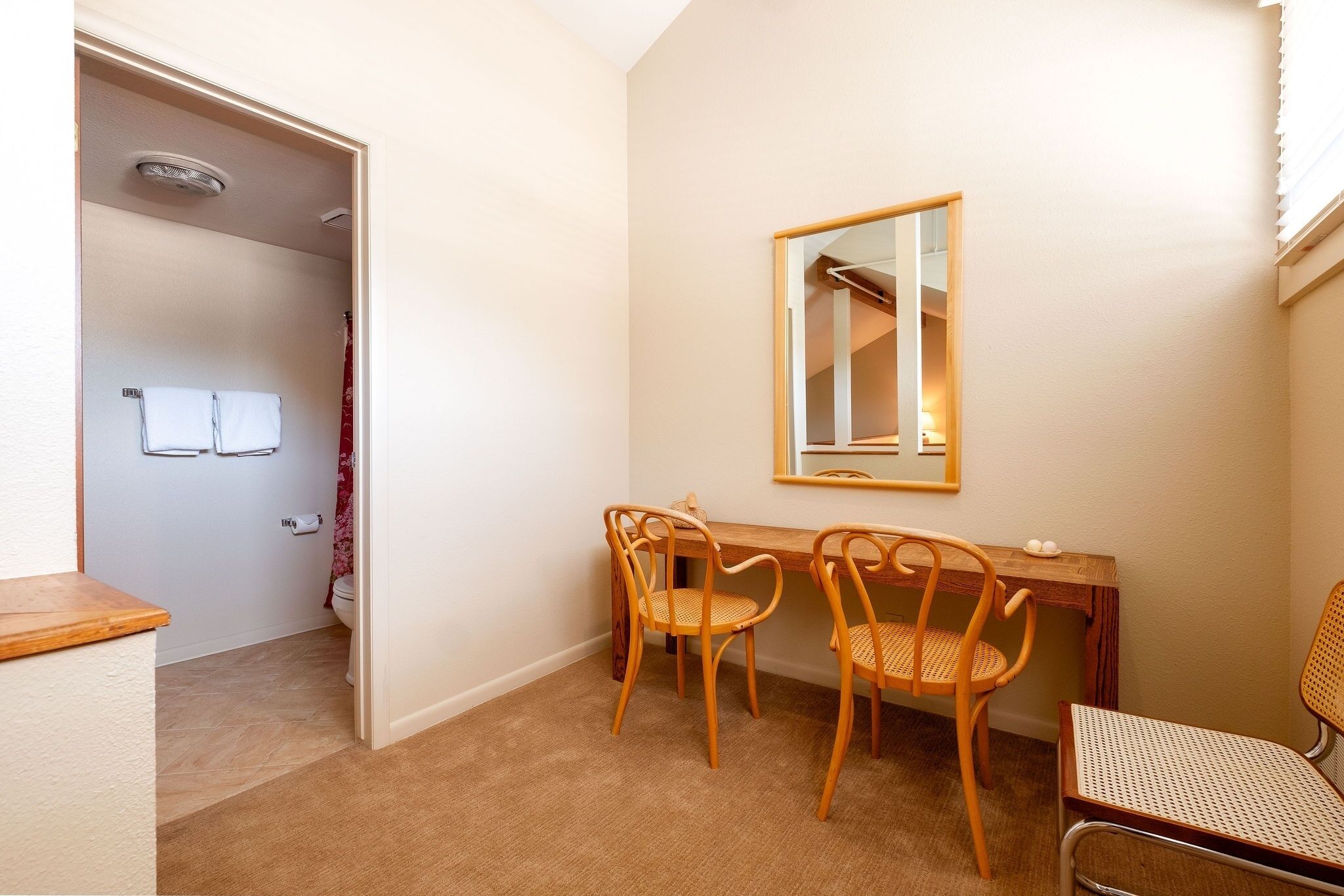 A compact room with a wooden desk, two chairs, a mirror, and a toilet.