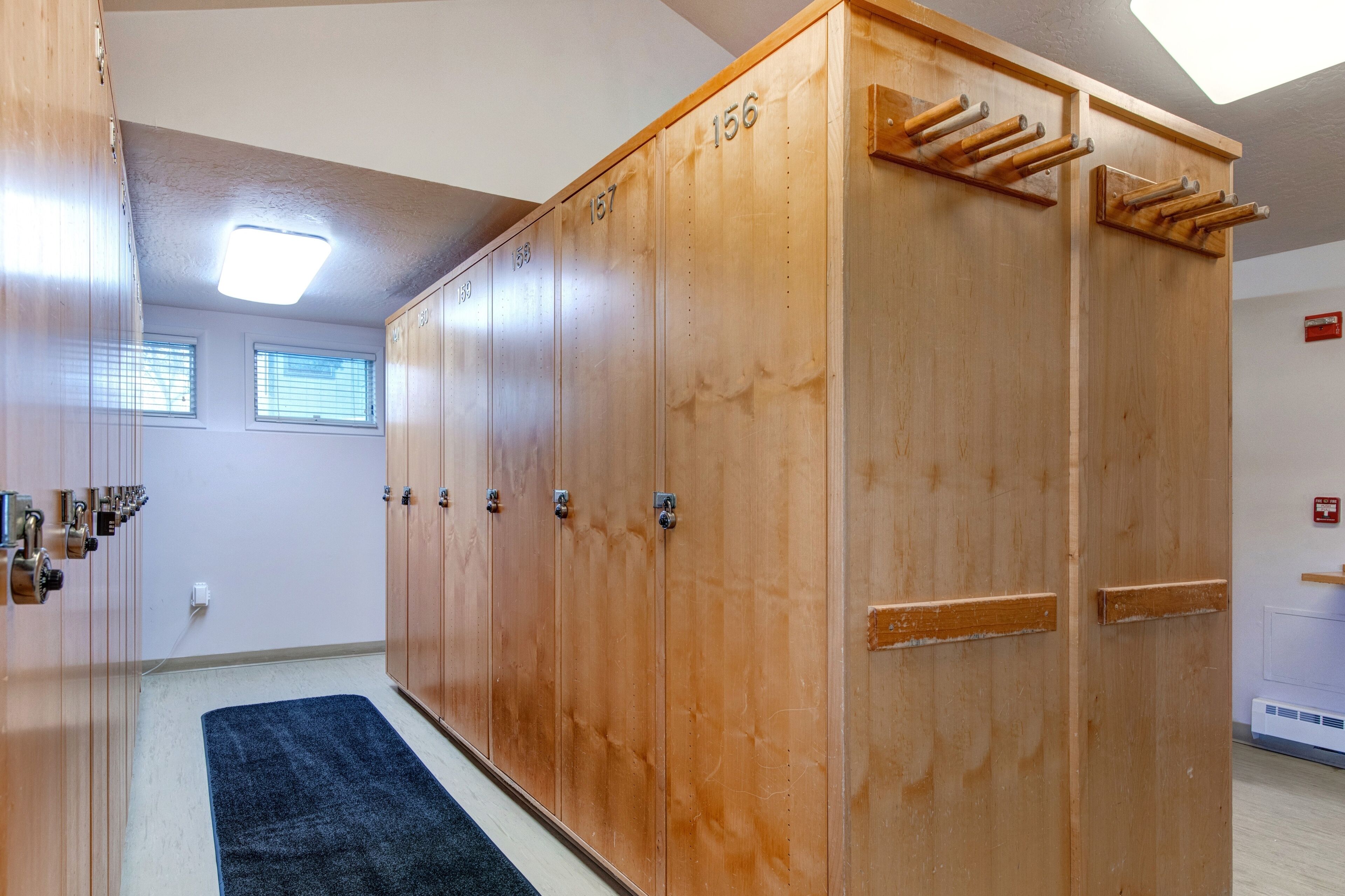 A row of wooden lockers with numbered doors, a blue carpet, and a ceiling light fixture.