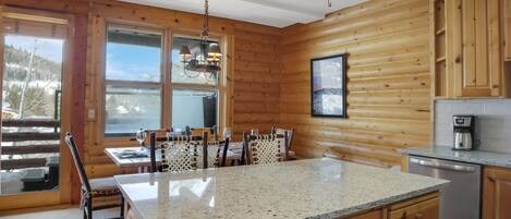 A log cabin interior with a kitchen, dining area, and large windows.