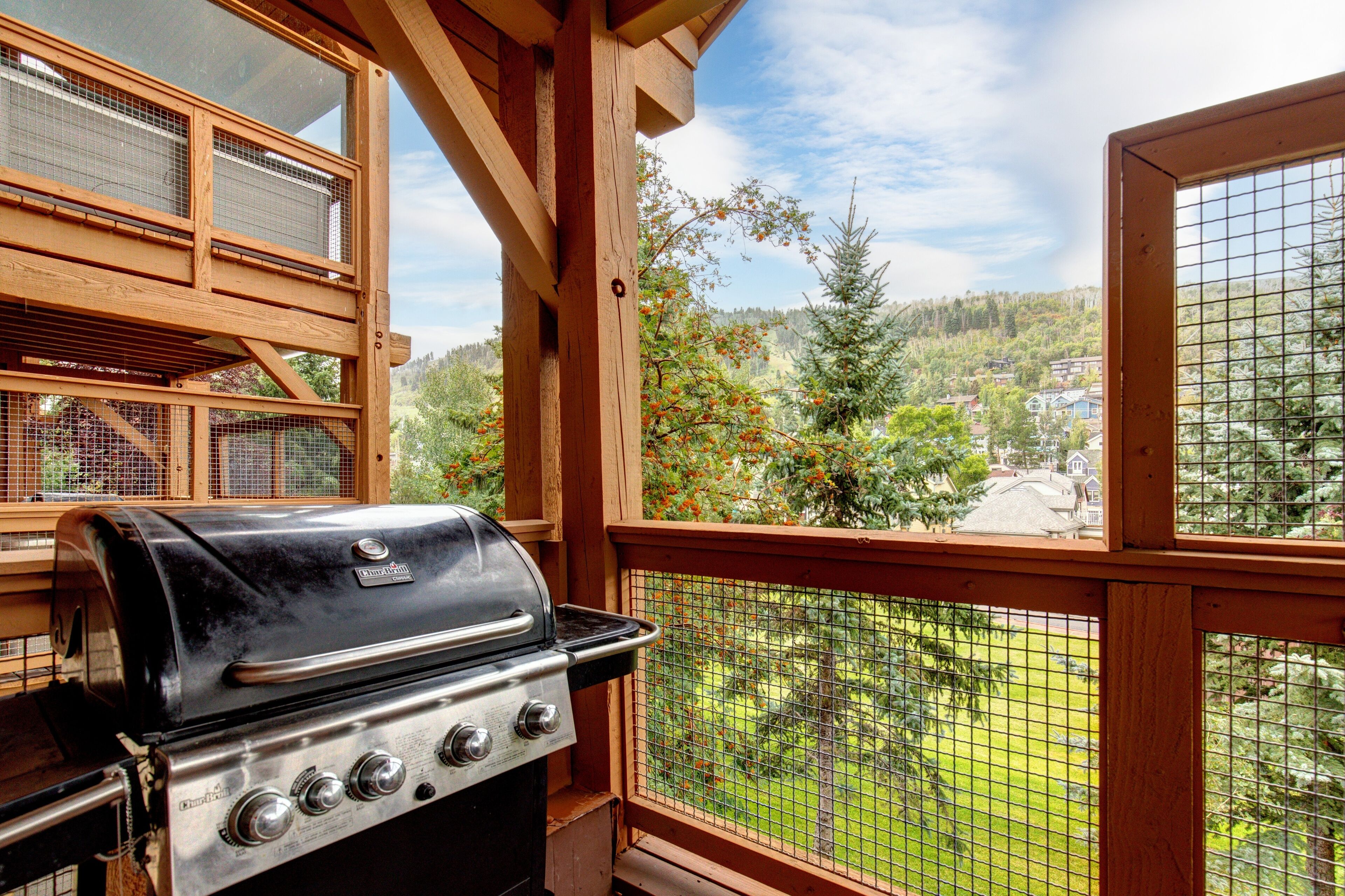 Una terraza de madera con una parrilla y vistas a un área boscosa.