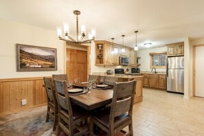 A spacious kitchen with wooden cabinets, a stainless steel refrigerator, and a dining area with a wooden table and chairs. - Snow Flower 055 2 Bedroom Condo by RedAwning (Park City)