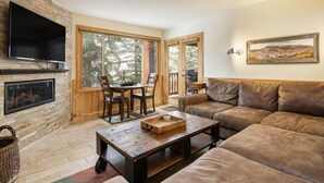 A cozy living room with a fireplace, a television, a sofa, and a dining area with chairs. - Snow Flower 055 2 Bedroom Condo by RedAwning (Park City)