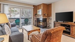 A living room with a fireplace, a television, a sofa, and a coffee table. - Snow Flower 147 2 Bedroom Condo by RedAwning (Park City)