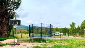A basketball court with a hoop and a netted enclosure, surrounded by greenery and a mountainous backdrop. - Maison de Campagne Avec Jardin (Cuers)