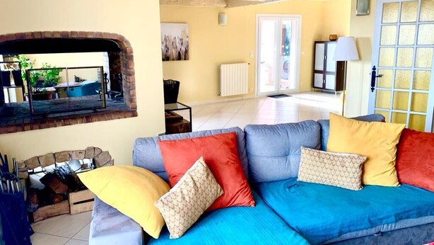 A living room with a blue sofa, red and yellow cushions, a fireplace, and a view of the outside. - Maison de Campagne Avec Jardin (Cuers)