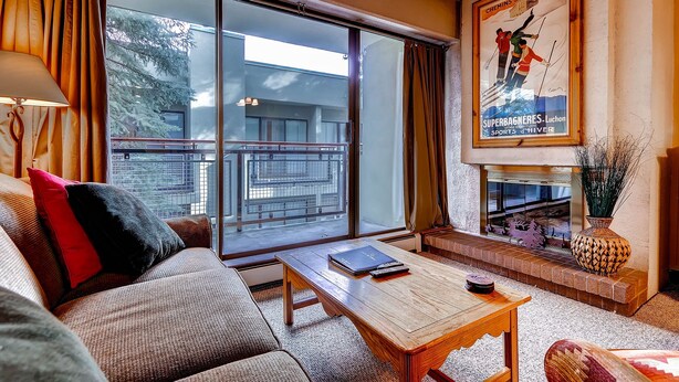A living room with a sofa, a coffee table, a fireplace, and a large window with curtains.