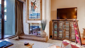 A living room with a large TV, a fireplace, a wooden cabinet, and a poster on the wall.