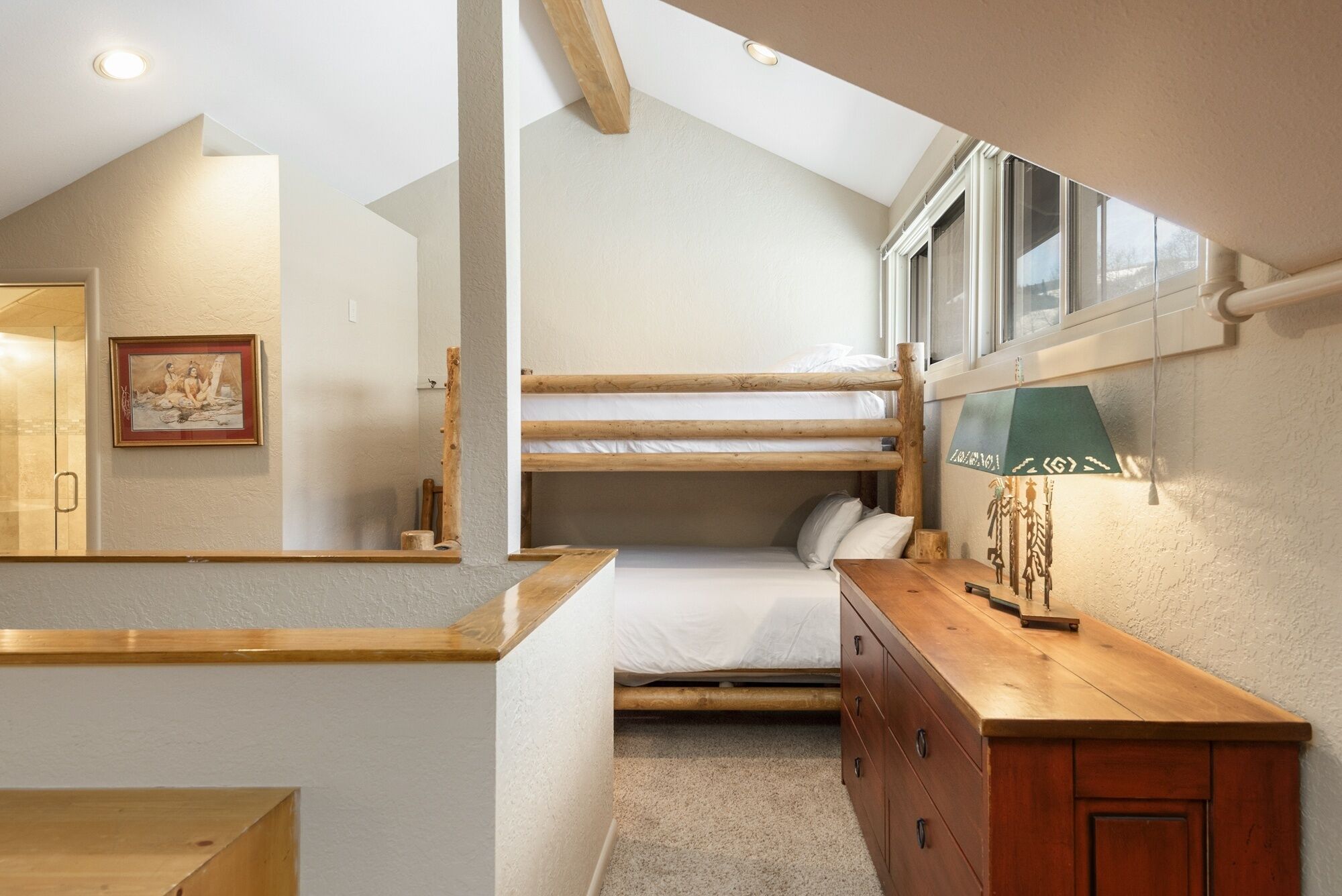 A compact bedroom with a bunk bed, a wooden dresser, and a framed picture on the wall.