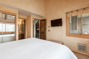 A bedroom with a large bed, a television mounted on the wall, and a window with curtains.