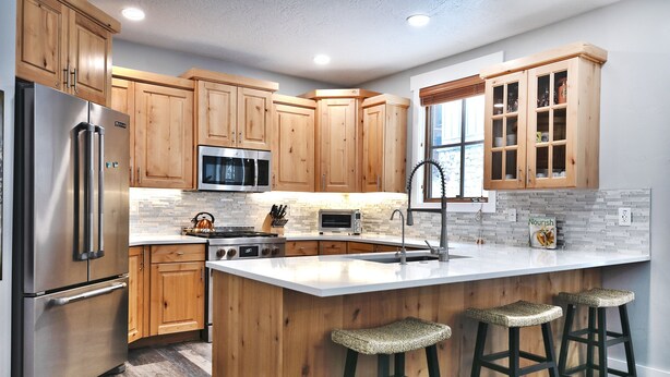 A modern kitchen with wooden cabinets, stainless steel appliances, a large island with bar stools, and a window with blinds.