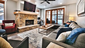 A living room with a stone fireplace, a red armchair, a large flat-screen TV, and a ceiling fan.