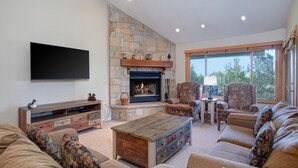A living room with a stone fireplace, a flat-screen TV, and a large window. - Snow Flower 028 3 Bedroom Condo by RedAwning (Park City)