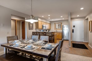 A modern kitchen with wooden cabinets, stainless steel appliances, and a dining area with a wooden table set for six. - Snow Flower 028 3 Bedroom Condo by RedAwning (Park City)