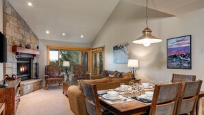 A cozy living room with a fireplace, comfortable seating, and a dining area set for a meal. - Snow Flower 028 3 Bedroom Condo by RedAwning (Park City)