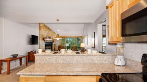 A modern kitchen with granite countertops, wooden cabinets, a built-in oven, a large window, and a stone fireplace. - Snow Flower 028 3 Bedroom Condo by RedAwning (Park City)