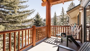 A wooden balcony with a view of snow-covered trees and a building in the background.
