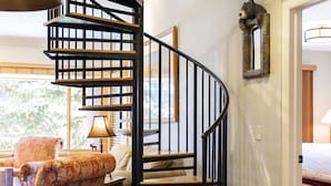 A spiral staircase with a wooden finish, a patterned armchair, a lamp, and a bear-shaped mirror on the wall.