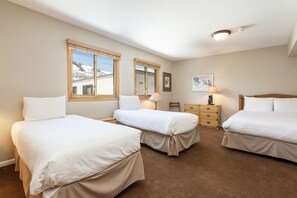 A bedroom with two single beds, a wooden dresser, a nightstand, and a window with a view of a snowy landscape. - Snow Flower 032 2 Bedroom Condo by RedAwning (Park City)