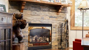 A stone fireplace with a log fire, surrounded by rustic decor including a bear sculpture and a wooden shelf with framed photos.