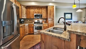 Una cocina moderna con armarios de madera, electrodomésticos de acero inoxidable, encimeras de granito y una isla integrada con lavabo.