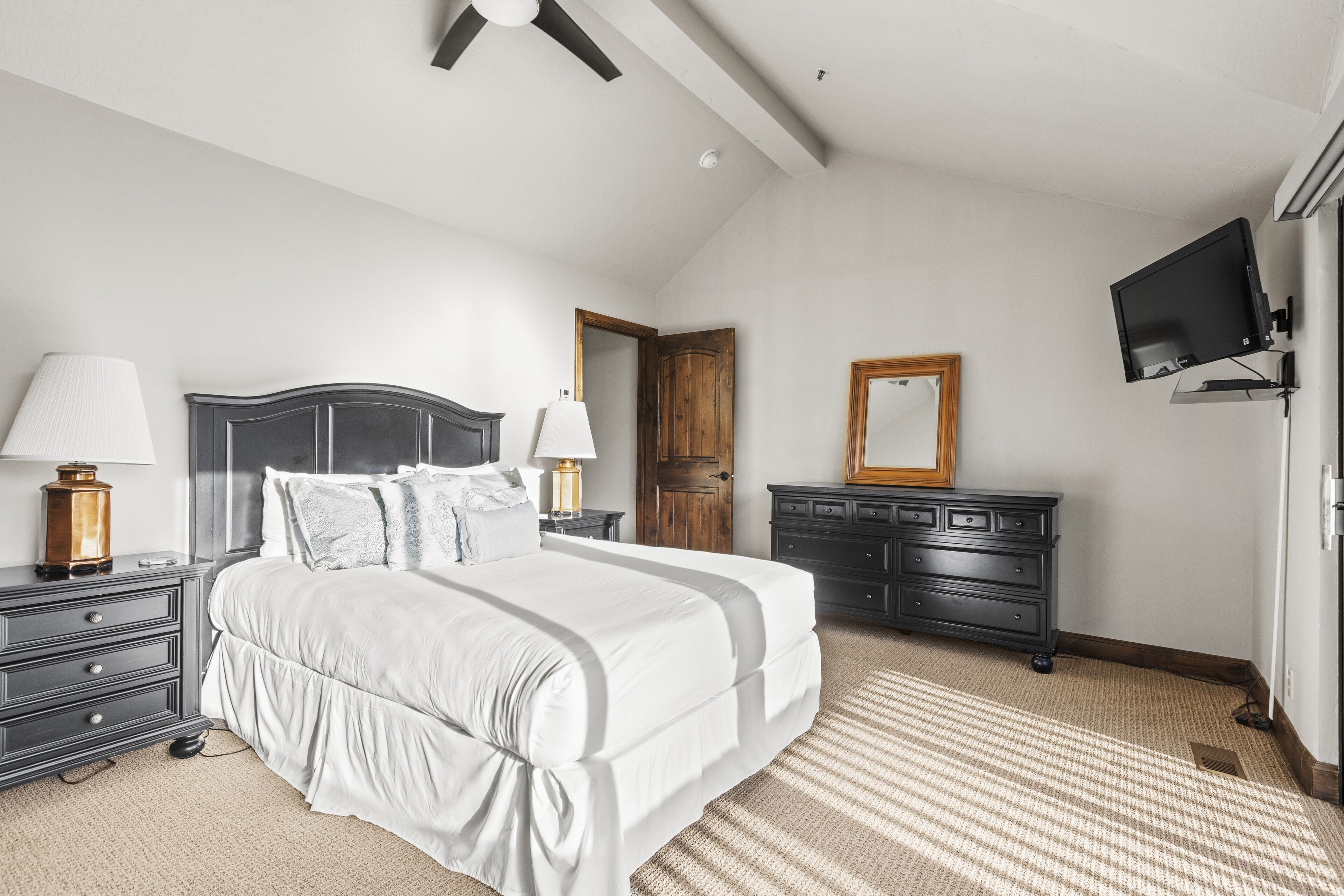 A bedroom with a large bed, a dresser, a television, and a ceiling fan.