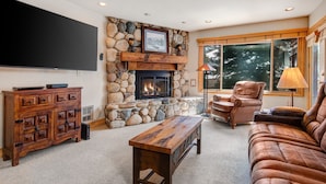 A living room with a stone fireplace, a flat-screen TV, a wooden coffee table, leather sofas, and a stone accent wall.