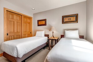 Ein Hotelzimmer mit zwei Einzelbetten, einem Holzschrank, gerahmten Bildern an der Wand und einem kleinen Tisch mit Lampe.
