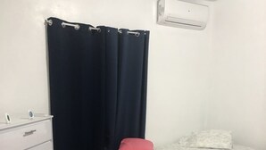Un dormitorio con cama, cómoda, ventana con cortinas y unidad de aire acondicionado.
