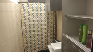 Un baño pequeño con inodoro, lavabo y cortina de ducha. Hay artículos de aseo en el lavabo y una alfombra en el suelo.