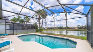 Una piscina con vista a un lago, rodeada por una zona techada con palmeras y casas al fondo.