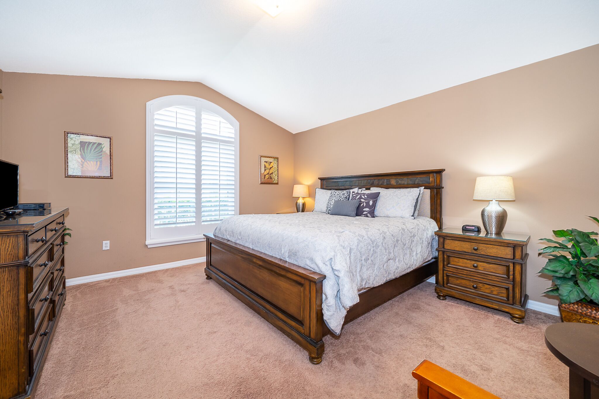 A bedroom with a large bed, two bedside tables, a dresser, and a window with blinds.