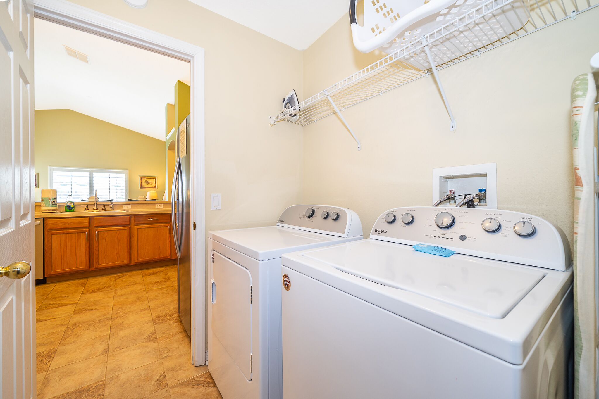 A laundry room with two front-loading washers and dryers, a drying rack, and a window with blinds.