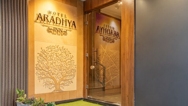 Entrada de hotel com relevo de árvore, plantas em vasos e área gramada que leva à porta.