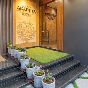 Entrada d'hotel amb un relleu de planta d'arbre, plantes en testos i una zona enjardinada que condueix a la porta.