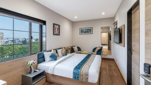 Quarto de hotel moderno com uma cama grande, uma mesa de cabeceira, televisão e vista para a cidade.