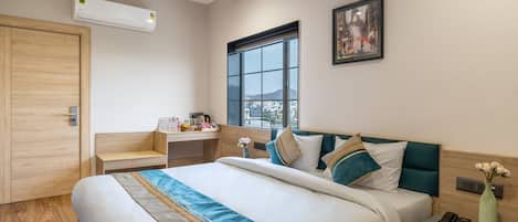 A modern hotel room with a large bed, a desk, a window with a city view, and an air conditioning unit.