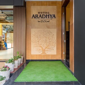 Entrada de un hotel con fachada de madera, un mural de un árbol y césped artificial verde.