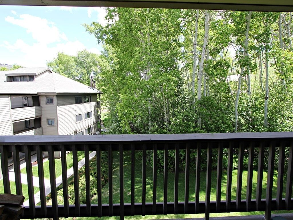 A balcony with a view of a residential area, including a house and a lawn.