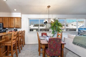 Enjoy a warm and inviting space with a large window offering a view of the surrounding landscape, a dining table for two, and a cozy seating area.