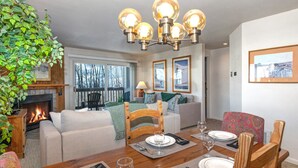 A dining area with a wooden table set for four, a fireplace, and a view of the outdoors.