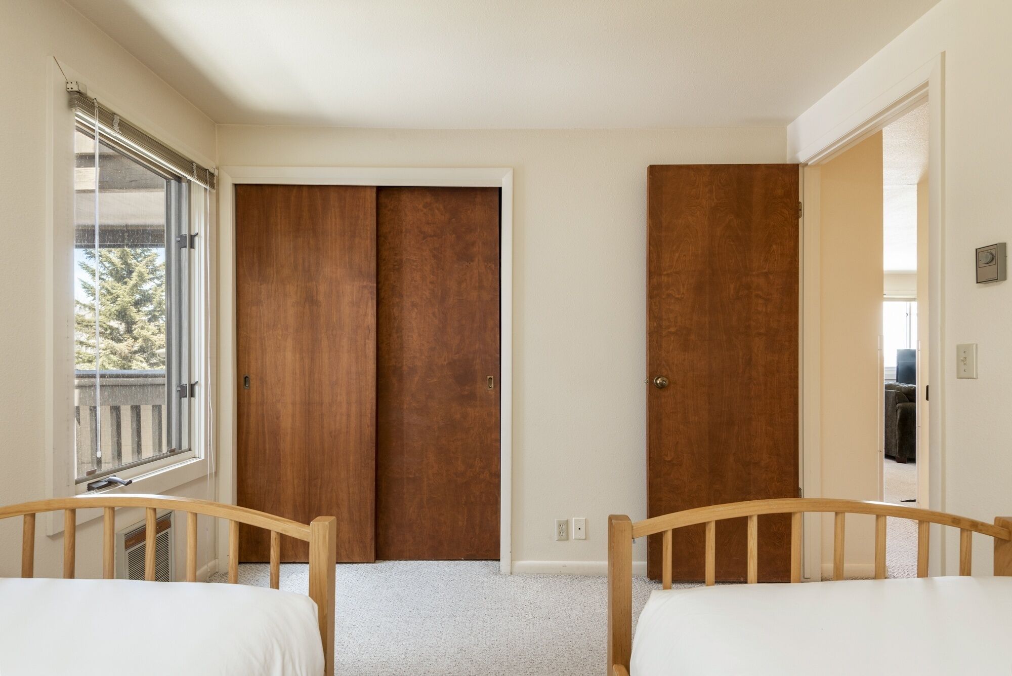 A bedroom with two wooden beds, a window with blinds, and a door with a mirror.