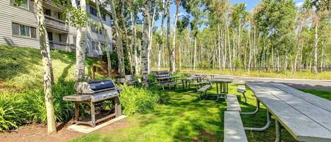 Un parque con mesas de picnic, una parrilla y un edificio con balcones.